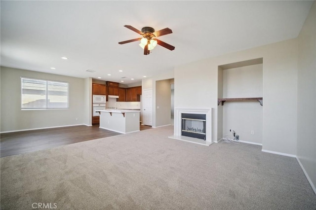 unfurnished living room featuring ceiling fan and dark colored carpet