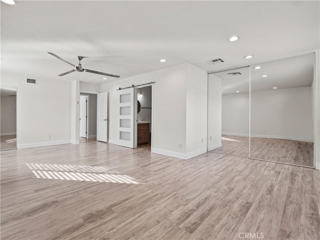 interior space with ceiling fan, a barn door, and light hardwood / wood-style flooring