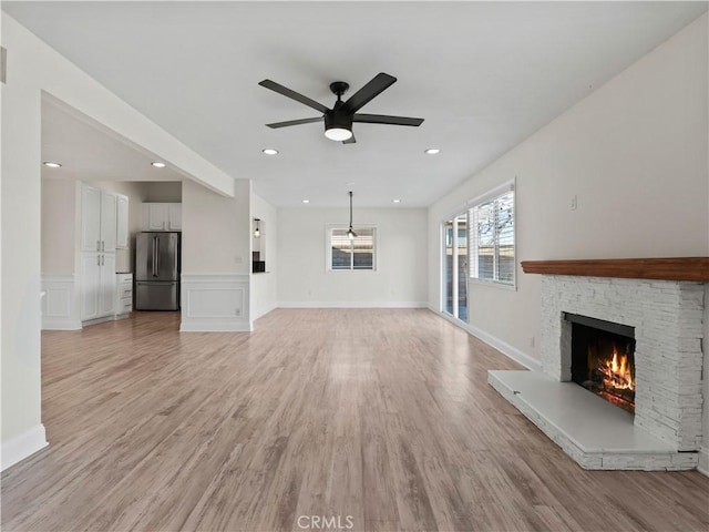 unfurnished living room with a stone fireplace, light hardwood / wood-style flooring, and ceiling fan