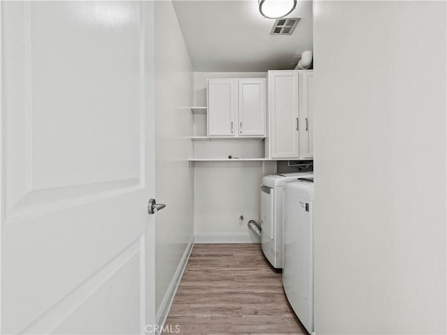 clothes washing area with cabinets, light hardwood / wood-style flooring, and washer and dryer