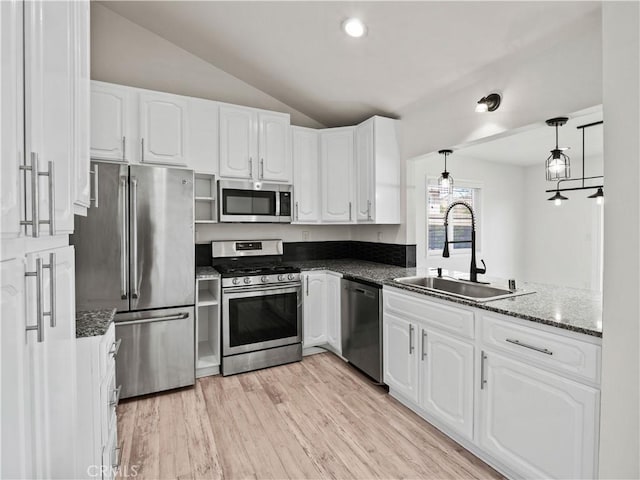 kitchen with sink, appliances with stainless steel finishes, white cabinetry, hanging light fixtures, and vaulted ceiling