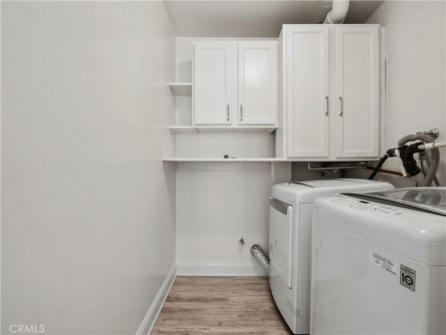 clothes washing area with cabinets, washing machine and dryer, and light hardwood / wood-style flooring