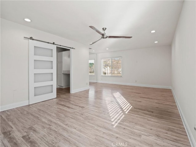 unfurnished bedroom featuring ceiling fan, a barn door, and light wood-type flooring