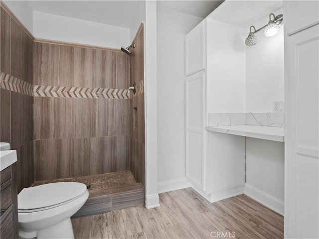 bathroom with hardwood / wood-style flooring, vanity, toilet, and a tile shower