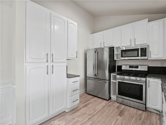 kitchen featuring dark stone countertops, vaulted ceiling, white cabinets, and appliances with stainless steel finishes