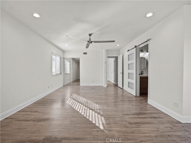 unfurnished room with a barn door, hardwood / wood-style floors, and ceiling fan