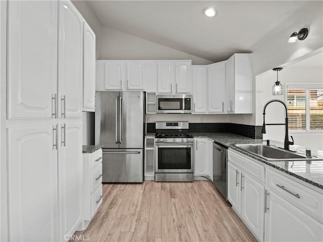 kitchen with lofted ceiling, sink, hanging light fixtures, stainless steel appliances, and white cabinets