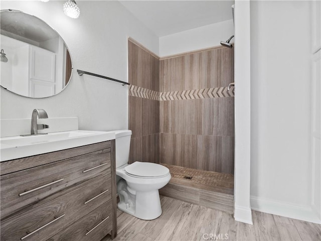 bathroom with hardwood / wood-style flooring, vanity, a tile shower, and toilet