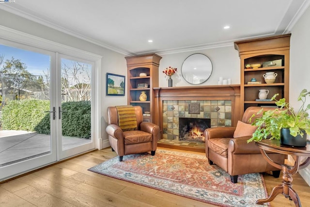 sitting room featuring french doors, ornamental molding, a fireplace, and light hardwood / wood-style floors