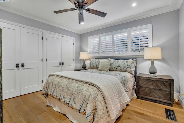 bedroom featuring crown molding, two closets, light hardwood / wood-style flooring, and ceiling fan