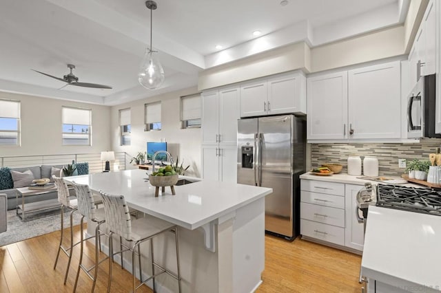 kitchen featuring appliances with stainless steel finishes, a breakfast bar area, white cabinets, hanging light fixtures, and a center island with sink