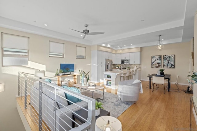 living room with a tray ceiling, ceiling fan, and light wood-type flooring