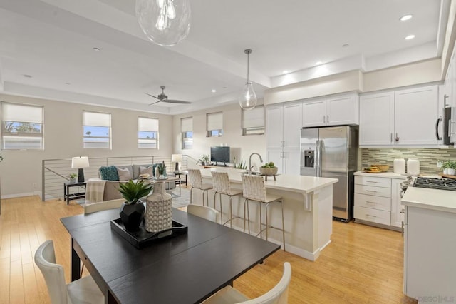 dining space with ceiling fan, light hardwood / wood-style floors, and a tray ceiling