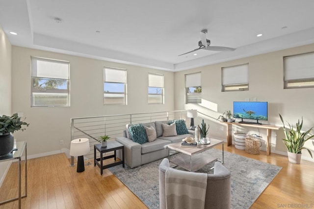 living room with ceiling fan, plenty of natural light, a raised ceiling, and light wood-type flooring