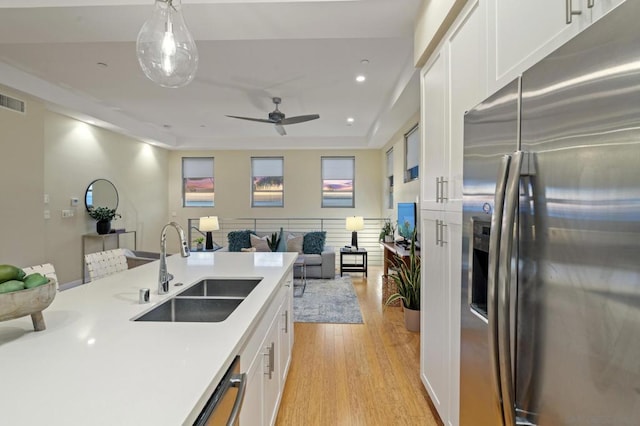 kitchen featuring sink, appliances with stainless steel finishes, white cabinetry, light hardwood / wood-style floors, and decorative light fixtures