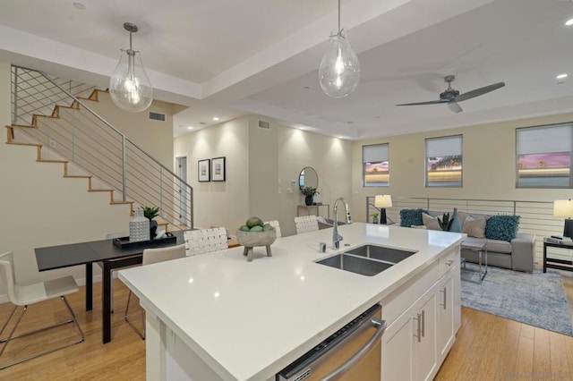 kitchen with sink, dishwasher, white cabinetry, hanging light fixtures, and an island with sink