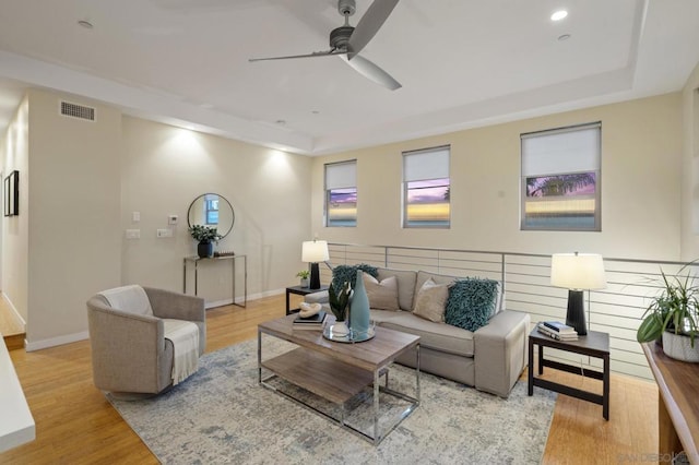 living room featuring ceiling fan, a tray ceiling, and light wood-type flooring