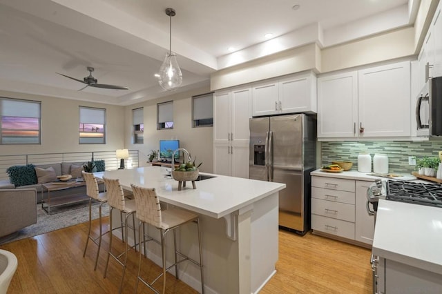 kitchen featuring a kitchen island with sink, decorative light fixtures, stainless steel appliances, and white cabinets