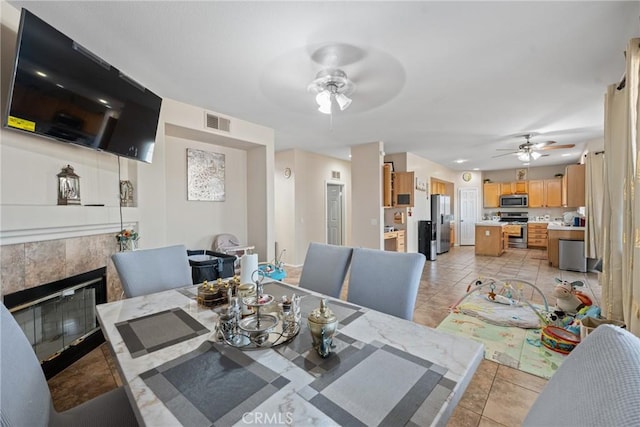 dining space featuring light tile patterned floors, a tile fireplace, and ceiling fan