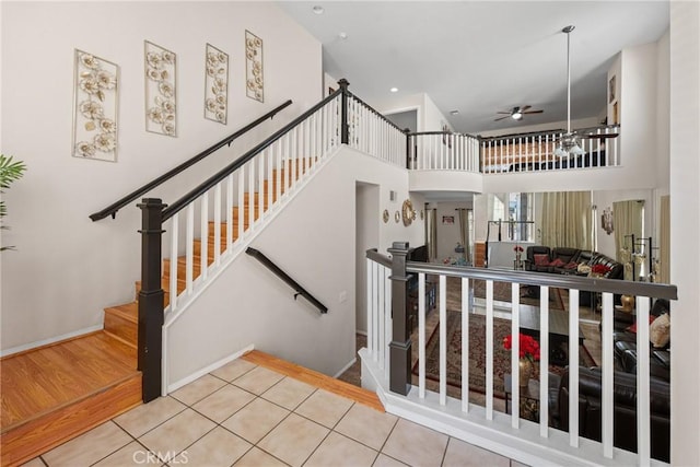 staircase with a towering ceiling, tile patterned floors, and ceiling fan