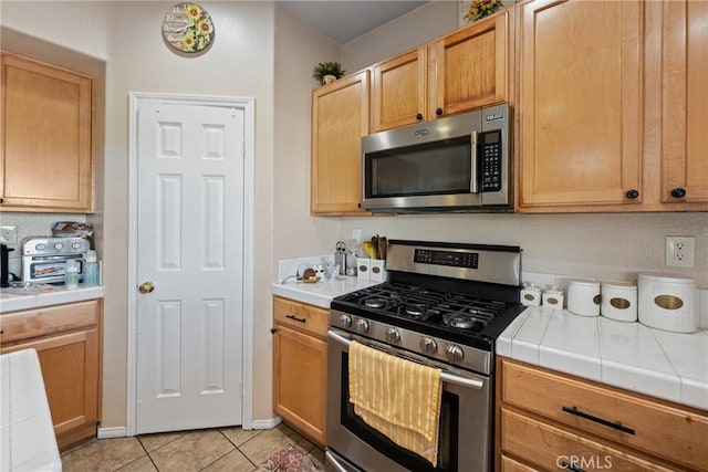 kitchen featuring light brown cabinetry, light tile patterned floors, tile counters, and appliances with stainless steel finishes