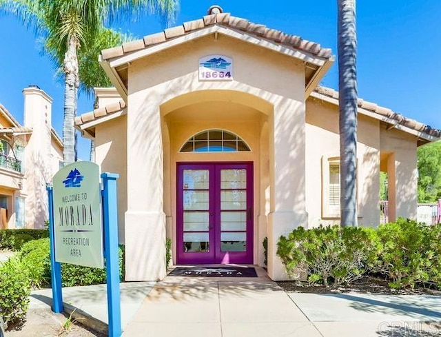 view of exterior entry featuring french doors, a tile roof, and stucco siding