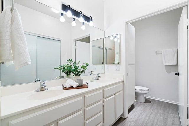 bathroom featuring double vanity, wood finished floors, a sink, and toilet