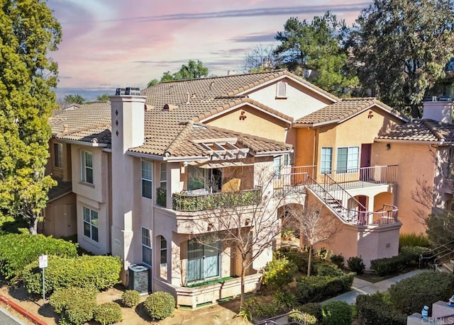 view of front of property featuring a tiled roof, central AC unit, a chimney, and stucco siding