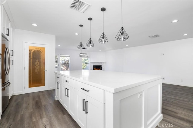 kitchen with hanging light fixtures, white cabinetry, a kitchen island, and stainless steel fridge