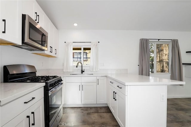 kitchen featuring sink, appliances with stainless steel finishes, white cabinetry, dark hardwood / wood-style flooring, and kitchen peninsula