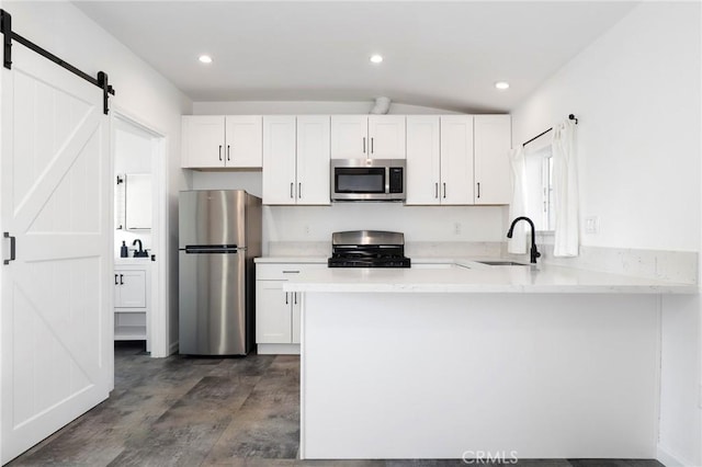 kitchen featuring sink, appliances with stainless steel finishes, white cabinetry, kitchen peninsula, and a barn door