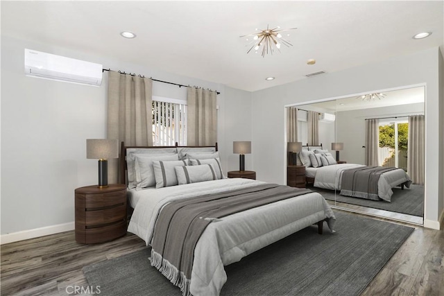 bedroom with dark wood-type flooring, a wall mounted AC, and an inviting chandelier