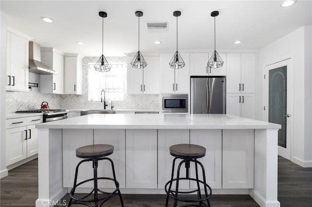 kitchen with white cabinetry, stainless steel appliances, wall chimney exhaust hood, and a kitchen island