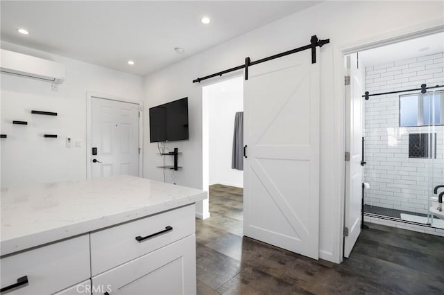 interior space featuring dark wood-type flooring, white cabinetry, a wall unit AC, a barn door, and light stone countertops