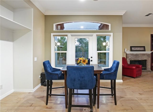 dining area with a fireplace, ornamental molding, and light hardwood / wood-style floors