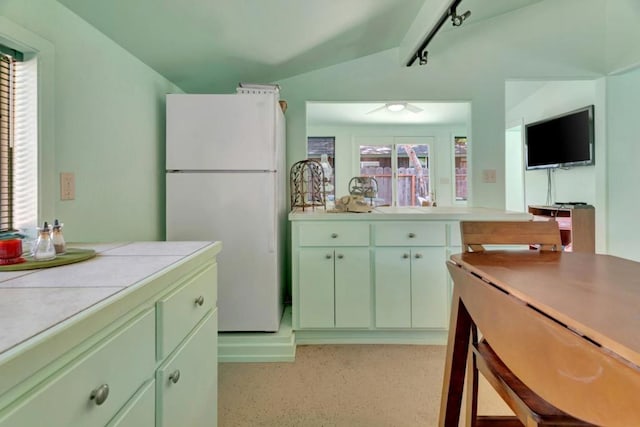 kitchen featuring vaulted ceiling, rail lighting, white fridge, tile counters, and green cabinets