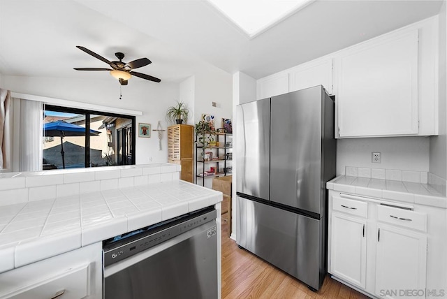 kitchen with stainless steel appliances, tile countertops, light wood-type flooring, and white cabinets