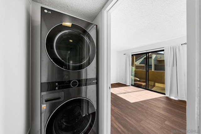 laundry area featuring stacked washer / dryer, wood-type flooring, and a textured ceiling