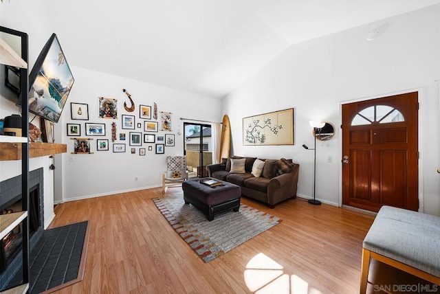 living room with high vaulted ceiling, a tile fireplace, and light hardwood / wood-style flooring