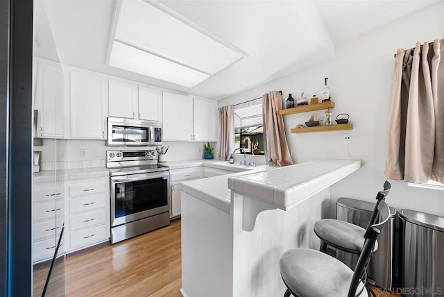 kitchen featuring a breakfast bar, stainless steel appliances, white cabinets, tile countertops, and kitchen peninsula