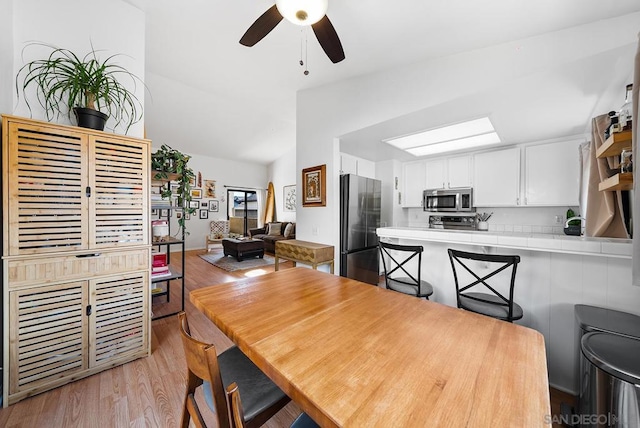 dining space featuring ceiling fan, lofted ceiling with skylight, and light hardwood / wood-style floors