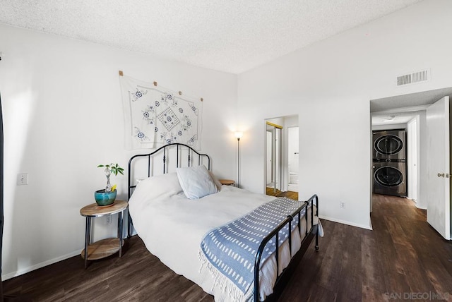 bedroom featuring stacked washing maching and dryer, dark hardwood / wood-style flooring, and a textured ceiling