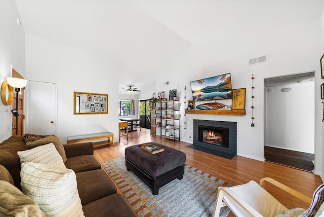 living room with ceiling fan, hardwood / wood-style floors, high vaulted ceiling, and a brick fireplace