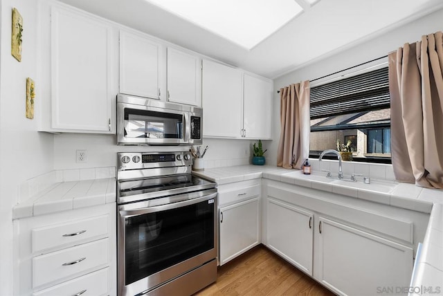 kitchen with stainless steel appliances, white cabinetry, sink, and tile countertops