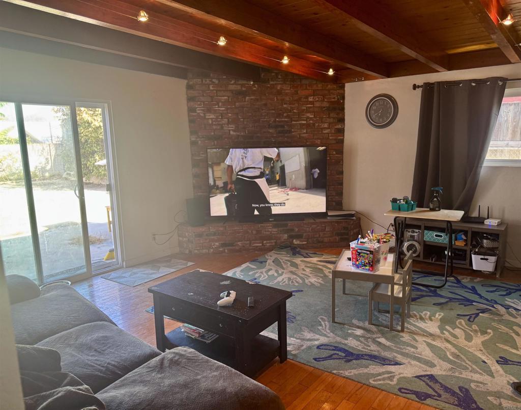 living room with wood-type flooring, lofted ceiling with beams, a brick fireplace, and wooden ceiling