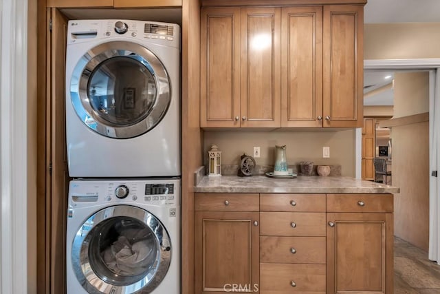 clothes washing area featuring cabinets and stacked washing maching and dryer