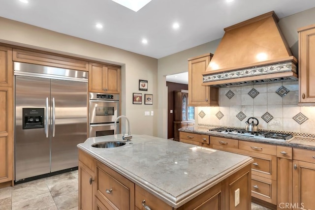 kitchen featuring sink, custom exhaust hood, stainless steel appliances, a kitchen island with sink, and backsplash