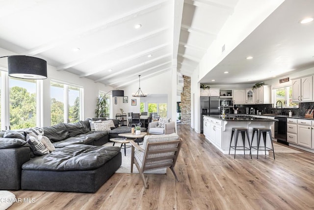 living room featuring sink, lofted ceiling with beams, light hardwood / wood-style floors, and a healthy amount of sunlight