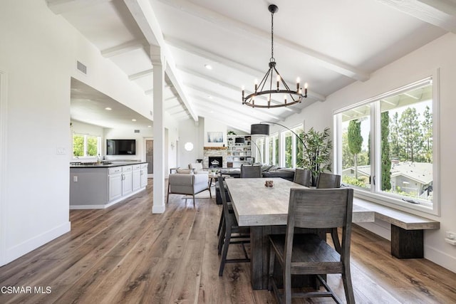 dining space featuring lofted ceiling with beams, wood-type flooring, a chandelier, and a fireplace