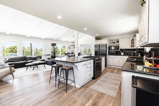 kitchen featuring vaulted ceiling with beams, a kitchen breakfast bar, a center island, black appliances, and white cabinets